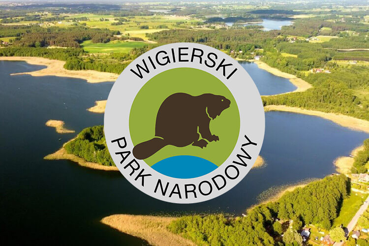 Zdjęcie przedstawia logo Wigierskiego Parku Narodowego na tle jeziora